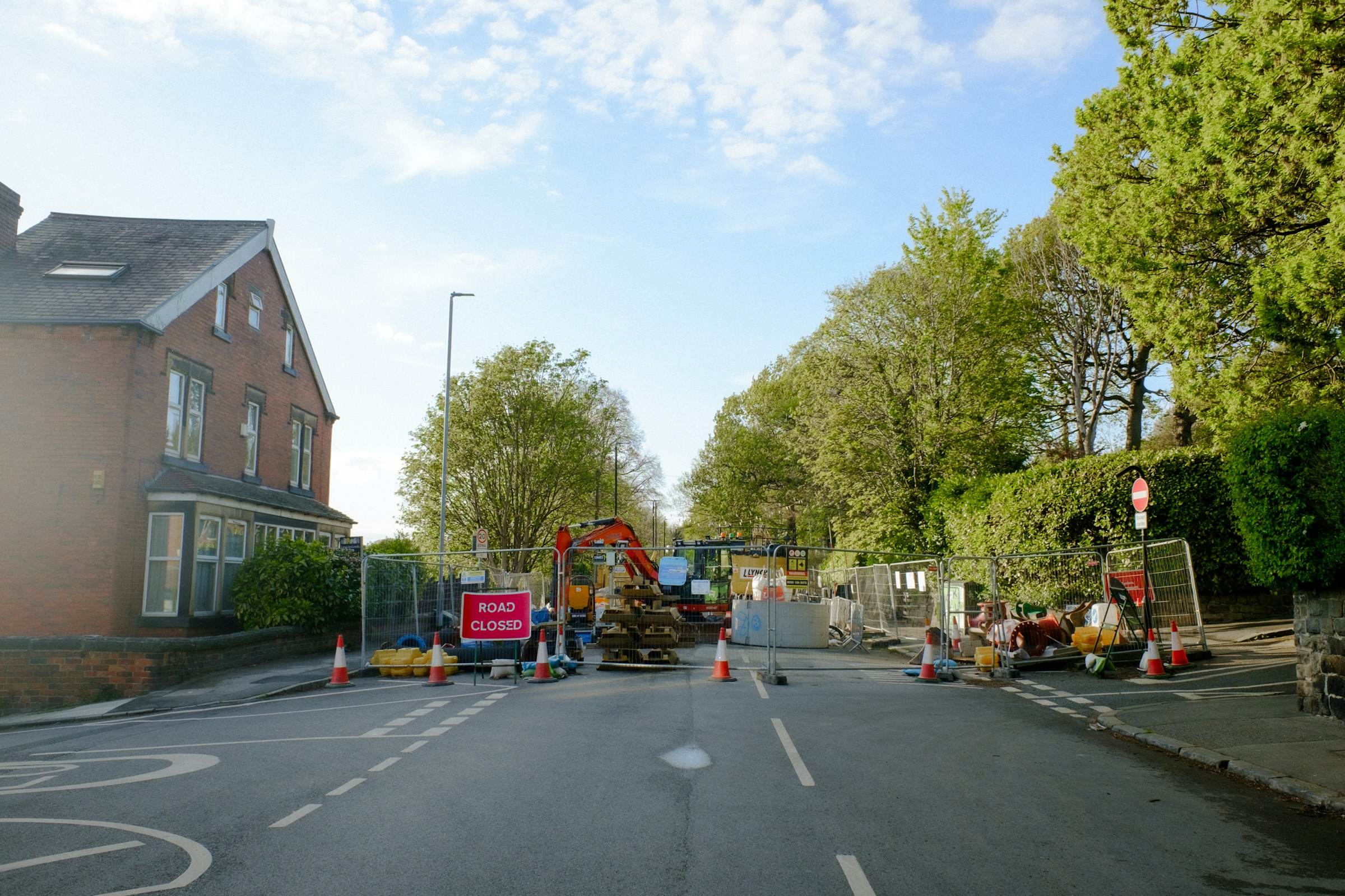Street works on a British road behind a road closed sign, with a mini excavator on site