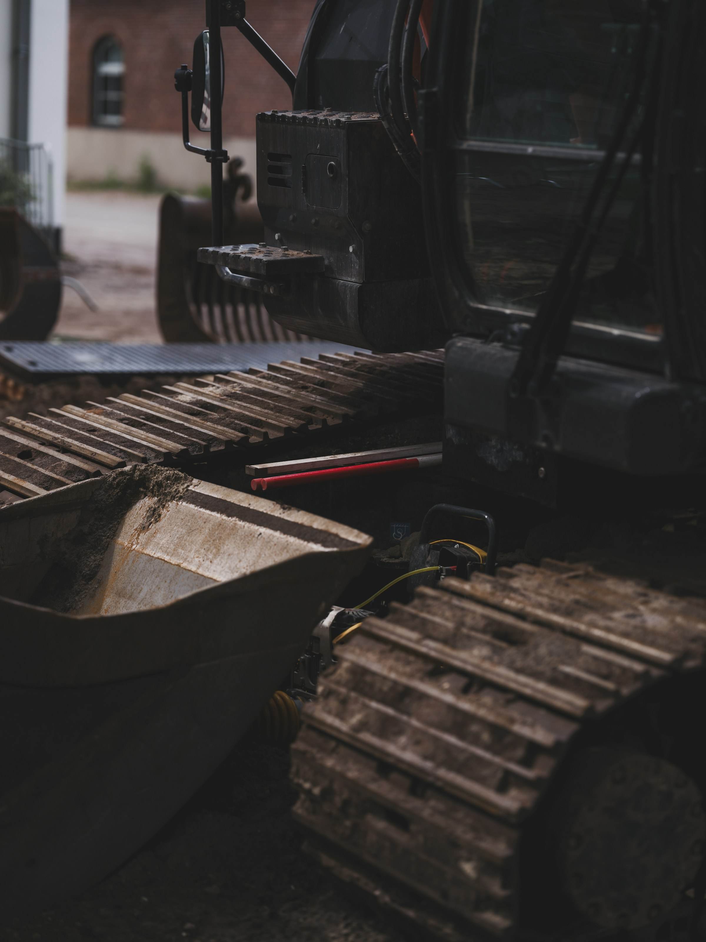 Close-up of muddy excavator tracks beside a bucket, in low light